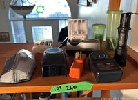 Photo shows multiple battery chargers, rechargeable AA batteries, battery adapters, and a black flashlight on a wooden surface.