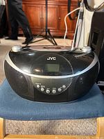 Front view of the black JVC portable CD player showing control buttons, LCD screen, and speakers.