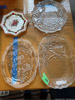 Four Christmas-themed serving plates and vintage crystal glassware arranged on wooden surface.