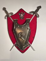 Full view of the metal chest armour plate mounted on red shield with crossed swords behind