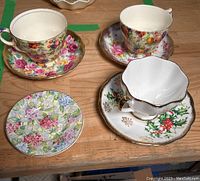 Four cups and saucers arranged on a wooden surface, showing different floral patterns and gold trims.