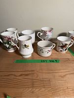 Front view of approximately 7 ceramic mugs with different floral designs arranged on a wooden surface.