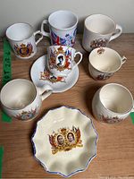 7 pieces shown including 6 mugs and one decorative scalloped edge plate all with royal portraits and British flags.