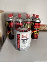 Primus and Mega Power gas canisters shown on a white surface, shrink wrapped Mega Power cans visible in background