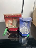 Two glass figurines in original packaging; left is angel with plaque, right is reindeer in blue box.