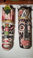 Both antique African masks shown side by side on a wooden surface, clear view of face details and paint colors.