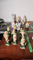 Front view showing seven green dwarf ceramic figurines along with assorted vintage hand painted figurines and two small painted vases.