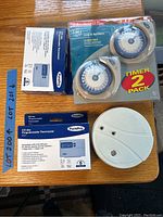 Photo showing two boxed PurePro programmable thermostats and a sealed pair of GE timers, and one white smoke alarm.
