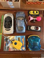 A group shot showing various die-cast cars, a vintage Barbie accessory horn in pink, a yellow remote control toy in packaging, a blue translucent toy car, and a remote control device.