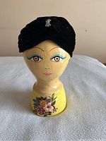 Front close-up of black vintage velour Art Deco ladies hat displayed on a stylized wooden model head with painted facial features and floral base decoration