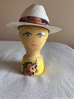 Beige Panama straw hat displayed on a yellow mannequin head with facial features and floral design on neck. View from front showing colorful patterned hat band.