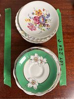 Stack of saucers with floral designs visible, showing a variety of colorful flowers including pink and purple with gold trim.