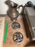 Vintage brass pitcher with handle showing patina and small dent, placed beside a stereo system