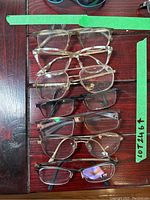 Top view of seven pairs of mixed style prescription eyeglasses laid out on dark wooden surface. Frames include plastic and metal in various colors and shapes.