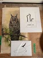Three unframed art works on wood floor, including a detailed owl watercolour and two bird prints