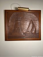 Frontal view of the wooden relief art frame featuring the lighthouse and sailboat with attached picture light.