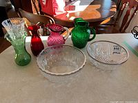 Overview of all glass bowls, pitchers, and vases on table in natural light.