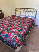 Bed made with brass headboard and colorful patchwork quilt, showing full bed and bedding.