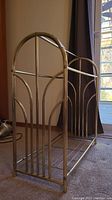 Side view of the brass quilt rack showing the tubular brass frame with arched decorative vertical bars and parallel rods on the bottom shelf.