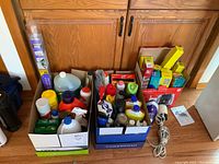 Overview of two boxes filled with assorted cleaning liquids and products, plastic wrap boxes stacked on the side.