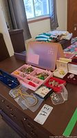 Wide view of assorted costume jewelry displayed on table including necklaces, brooches, earrings in compartment boxes and jewelry cases