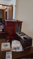 Wooden jewelry box with multiple drawers and mirrored door shown next to metal storage tin on a dresser, with some jewelry pieces visible.