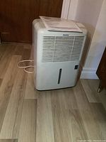 Full side view of Danby dehumidifier standing on floor with manual on top