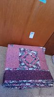 Folded quilt showing pink and purple floral patchwork design.