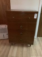Front view of wood dresser with four drawers and metal pull handles, showing overall condition and style.