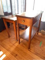 Two vintage wooden end tables shown side by side in natural light on hardwood floor, highlighting their size and finish.