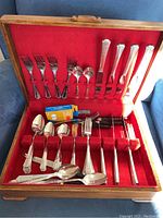 View of the full flatware set inside a wooden cutlery canteen lined with red felt, showing multiple forks, spoons, knives with bone handles, and other assorted utensils.