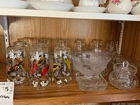 View of the entire glassware set showing ten painted bird water glasses, two pedestal bowls, glass coasters, and crystal sugar bowl.