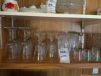 Shelf with clear stemmed wine glasses, vintage cut-patterned wine glasses, textured water glasses, and colorful vintage shot glasses.