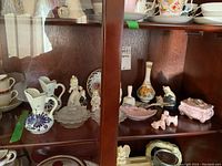 Photograph of knick knacks inside a wooden display cabinet including Delft vases, glass bowls, figurines, and decorative items.