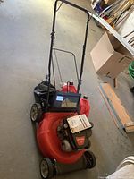 Full view of red Craftsman lawn mower with handlebar and wheels, showing overall condition and included items in background.