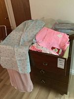 Vintage nightgowns, slips, aprons, tea towels, and other linens displayed in and over a wooden chest of drawers.