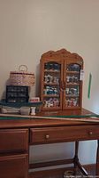 Full view of wood wall cabinet filled with assorted thread spools on a wooden surface with wicker sewing basket and button organizer beside it, with meter sticks in front.
