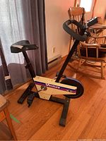 Full view of the stationary bike showing the seat, handlebars with digital gauge, pedals and floor stabilizers in a room with hardwood flooring.