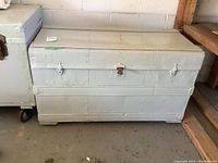 Full view of white painted metal steamer trunk showing front and side with latch hardware.