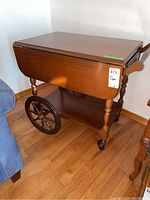 Side view of the tea wagon showing the drop leaf in lowered position and large rear wooden spoked wheel.