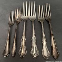 Full view of six mixed sterling silver forks with various designs and patina.