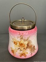 Front view showing pink and white gradient ceramic biscuit barrel with floral decoration and EPNS metal lid and handle.