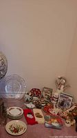 Photo of glass plates, mugs, small ceramic figurines including snowmen, boxed Christmas cards, and holiday napkins arranged on the floor against a plain wall.