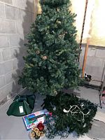 Full view of assembled artificial Christmas tree with stand, ornaments, and lights laid on floor nearby.