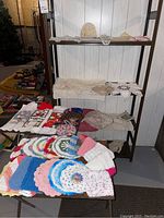 Shelf displaying cream and white lace doilies along with colorful knitted items on adjacent shelves and table