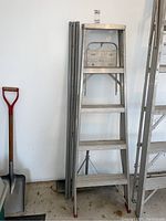 Photo showing the 4-foot aluminum folding ladder next to three aluminum poles and a snow shovel handle below.