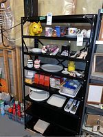 Front view of black metal shelving unit with various household items on shelves for size reference.