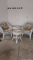 Full patio set with two white wicker chairs with floral cushions and two round wicker tables.
