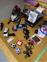 Overview of Polaris RC snowmobile with rider, multiple RC cars, remotes, Airship 1 balloon box, wheels, and manuals spread on floor