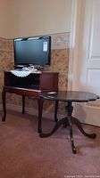 Room corner with dark wood TV stand holding a flat screen TV and an oval pedestal table in front of a white door.